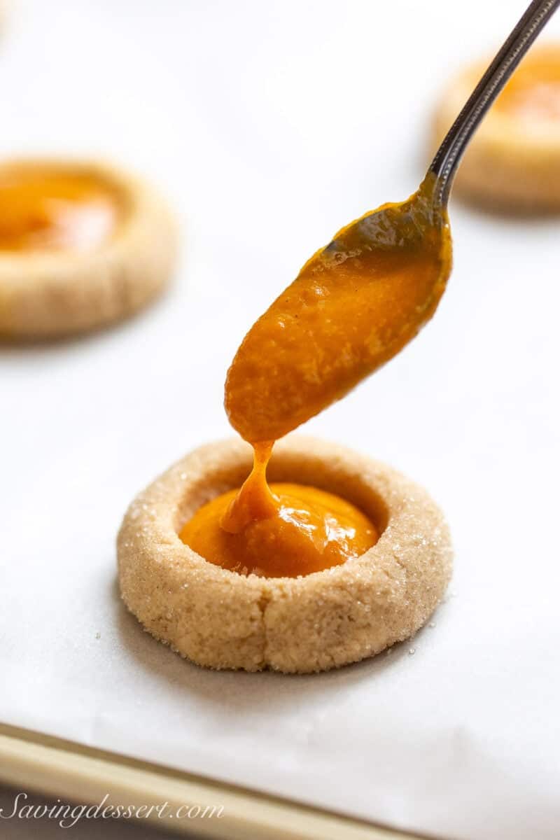 An unbaked cookie with a well in the center being filled with a spoonful of pumpkin pie filling.