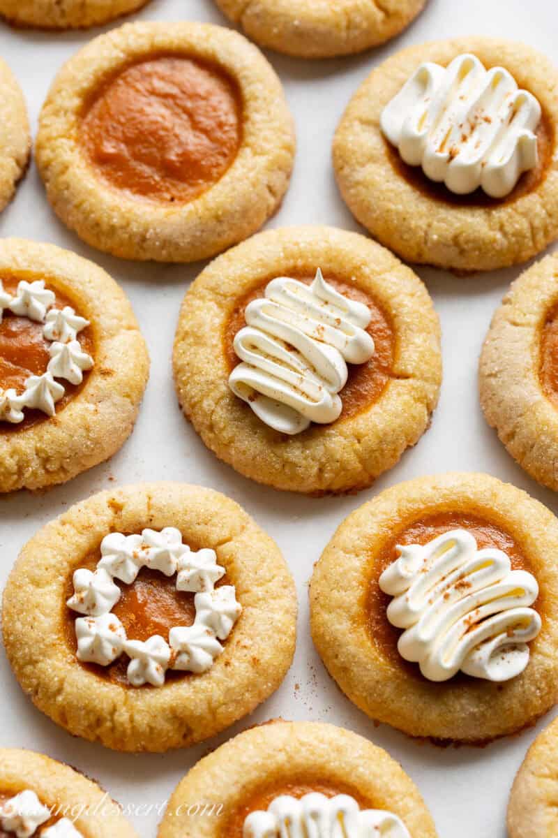 An overhead view of a tray filled with pumpkin pie filled cookies with some decorated with whipped cream.