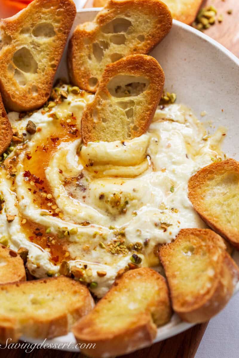 A slice of toasted baguette being dipped in creamy feta dip.