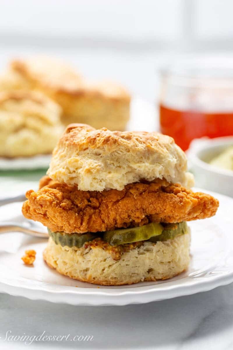 A big cat-head biscuit on a plate topped with a friend chicken fillet.