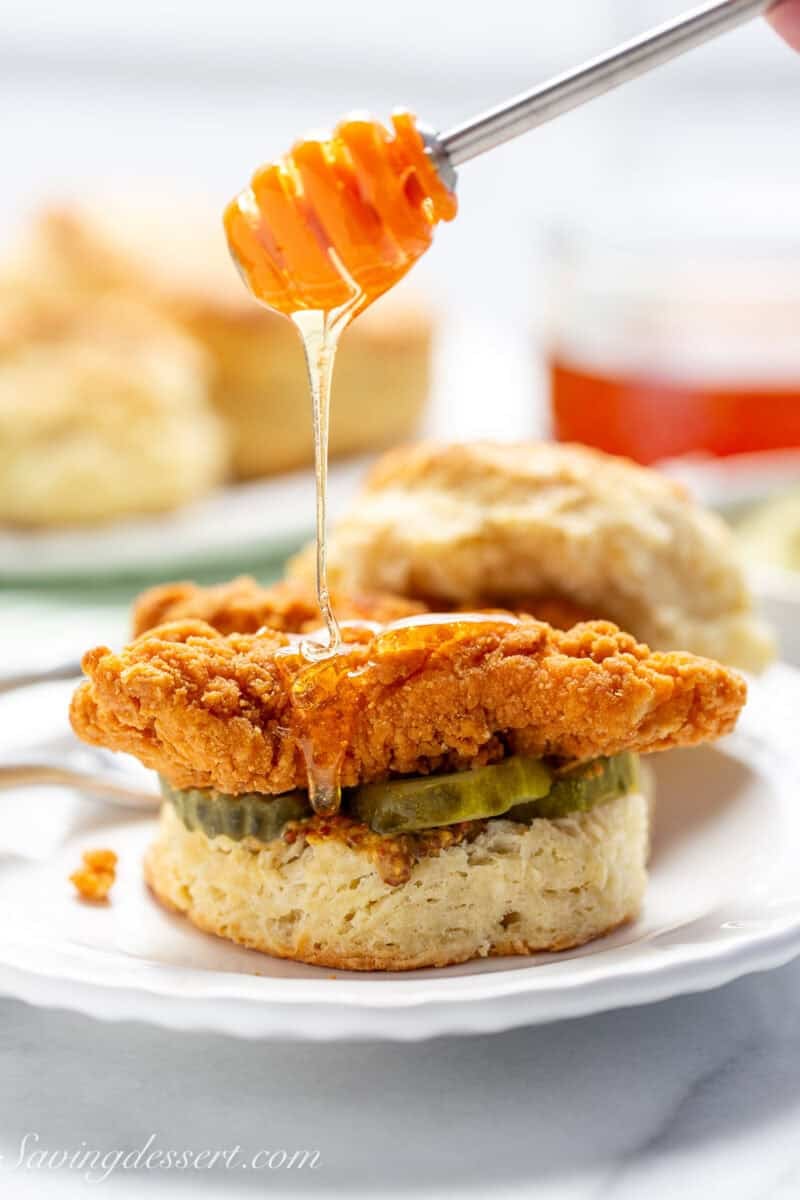 A piece of fried chicken on a biscuit being drizzled with honey.