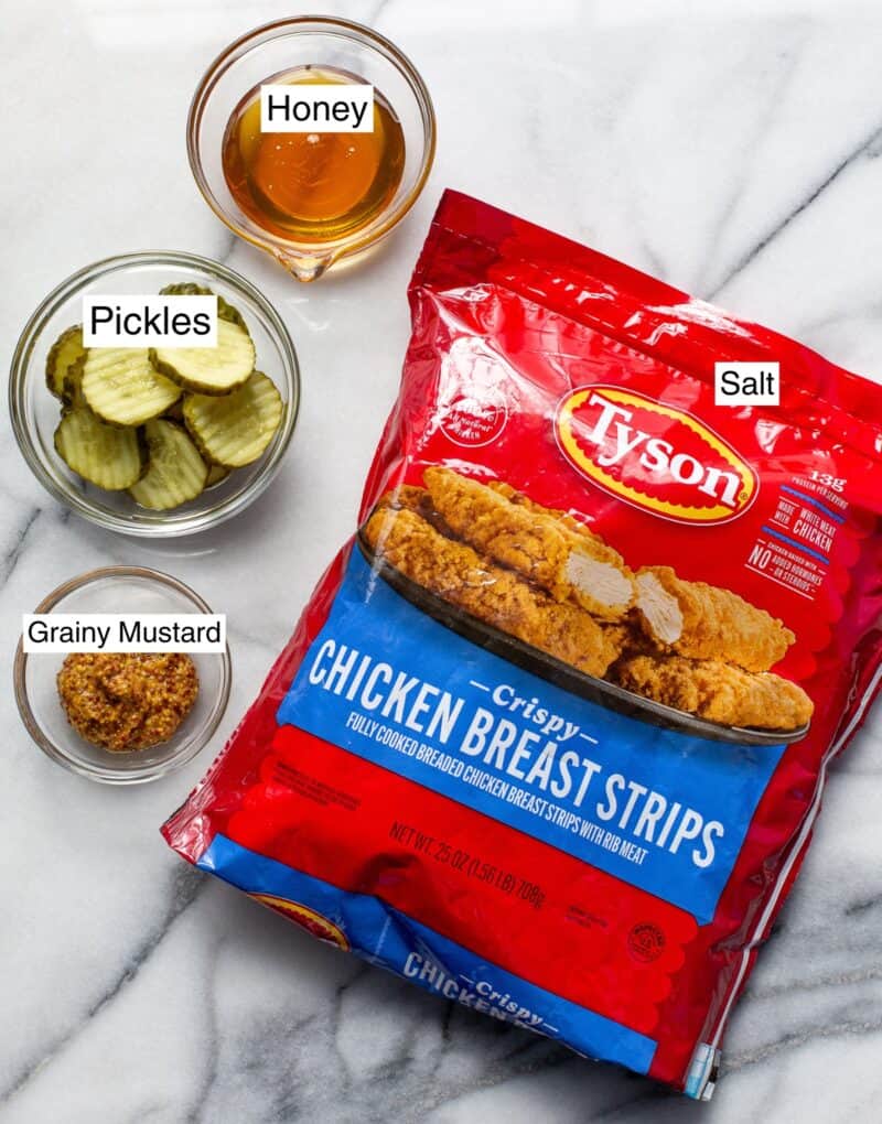 An overhead shot of frozen chicken strips, mustard, pickles and honey.