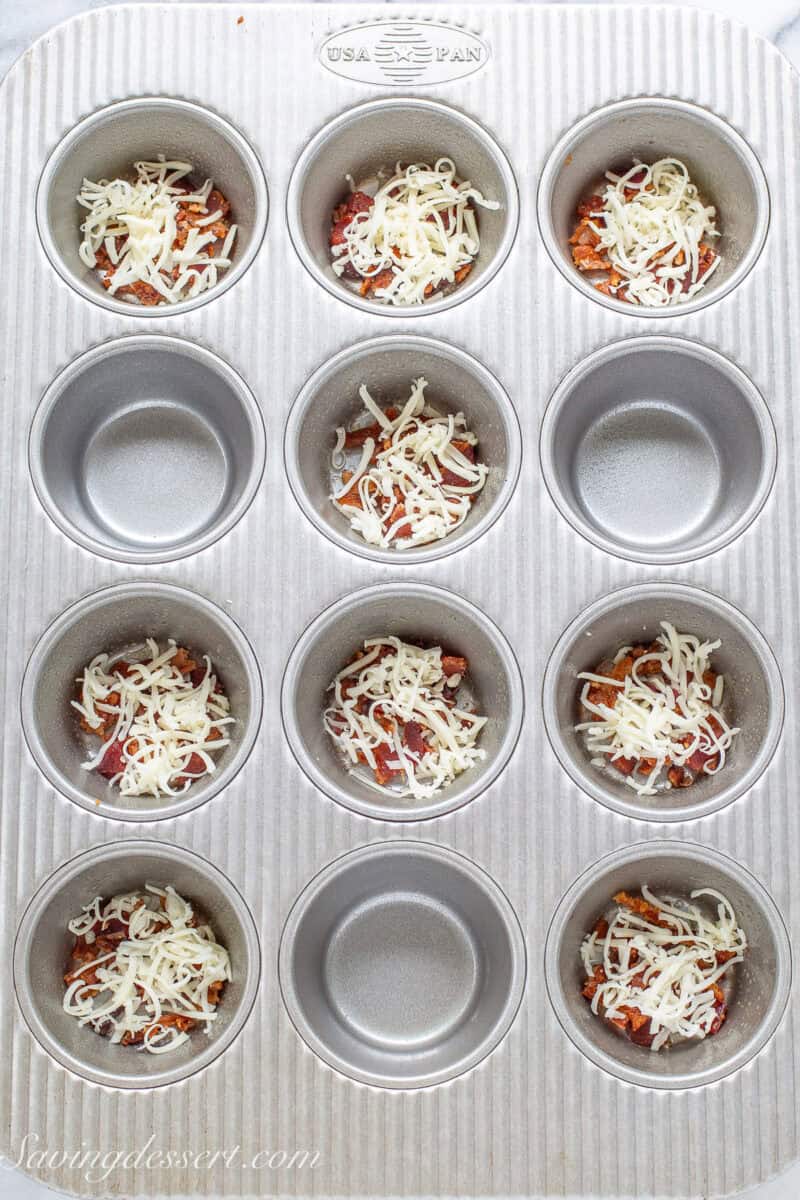 A muffin tin with bacon and cheese in the bottom of nine wells.