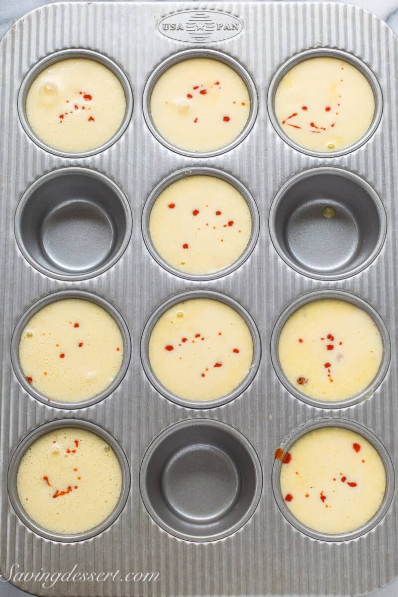 Egg muffin mixture in a muffin tin with hot sauce dripped on top.