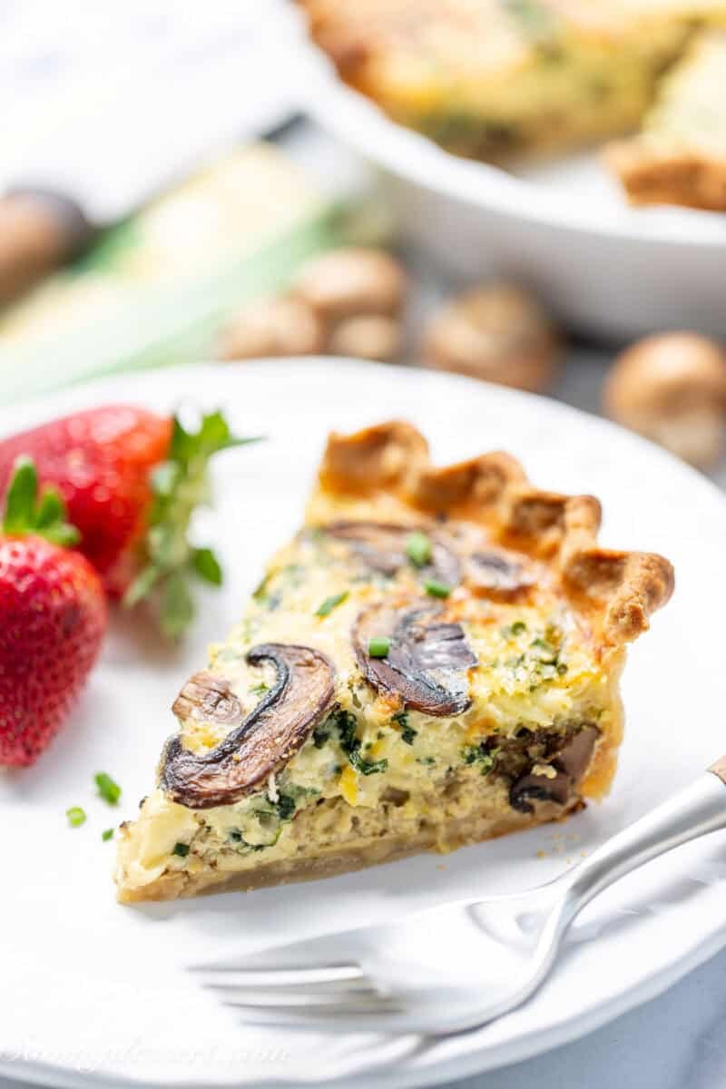 A slice of spinach mushroom quiche on a plate with strawberries on the side.