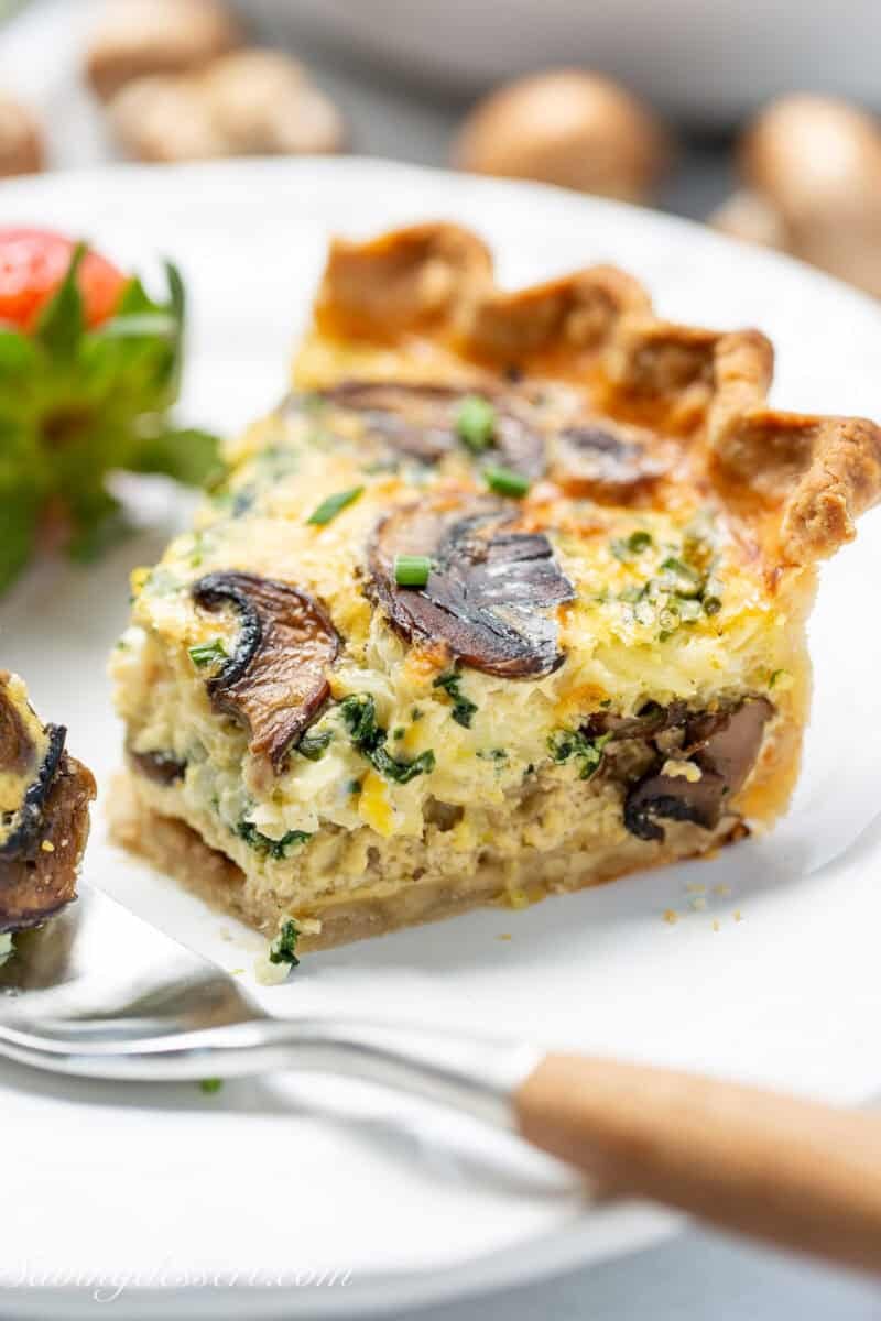 A slice of spinach mushroom quiche on a plate with a bite cut from the end.