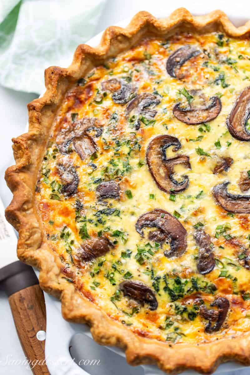 A close up on a spinach mushroom quiche with sliced mushrooms on top.