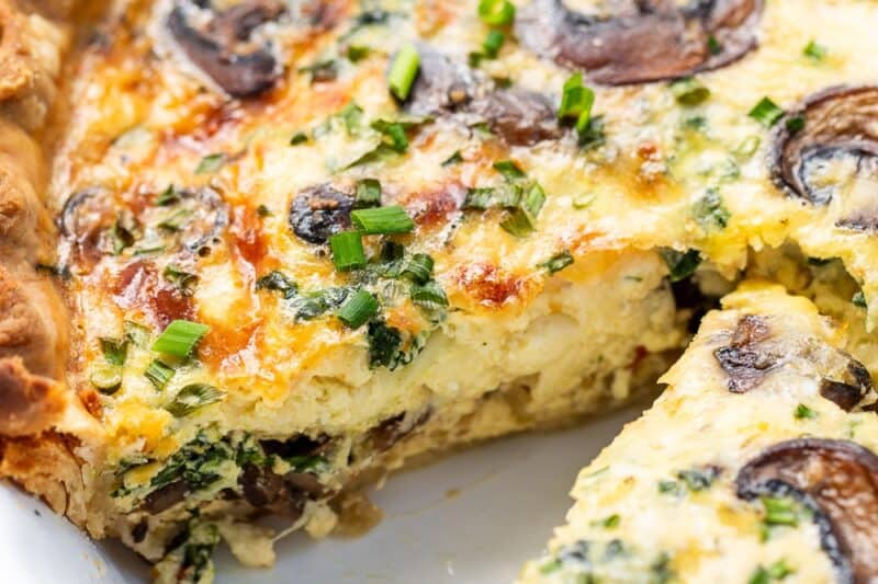A closeup on a sliced quiche with spinach and mushrooms.