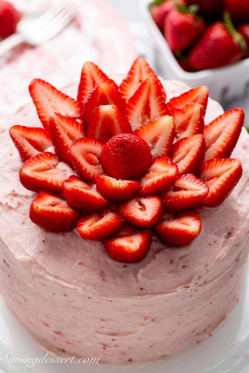 An overhead view of a strawberry cake with fresh strawberries halved and placed in a flower design.