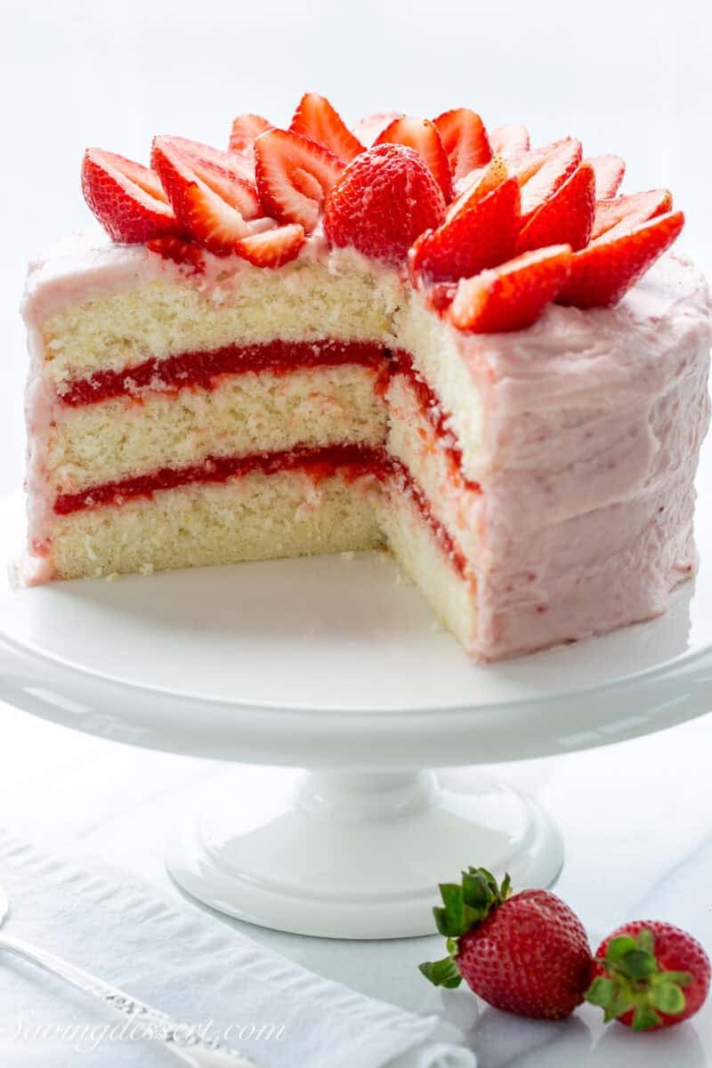 A partially sliced strawberry lemonade cake showing a bright pink strawberry filling between layers.