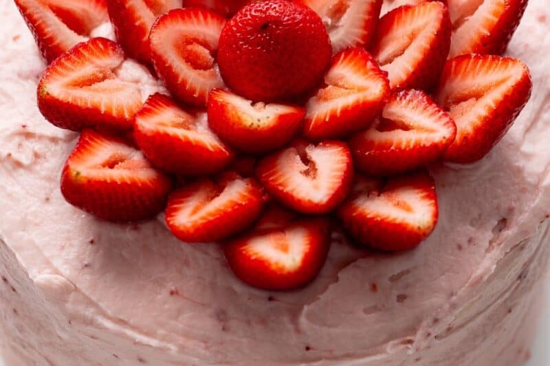 An overhead view of a strawberry cake topped with whole strawberries cut in half and arranged in a flower design.