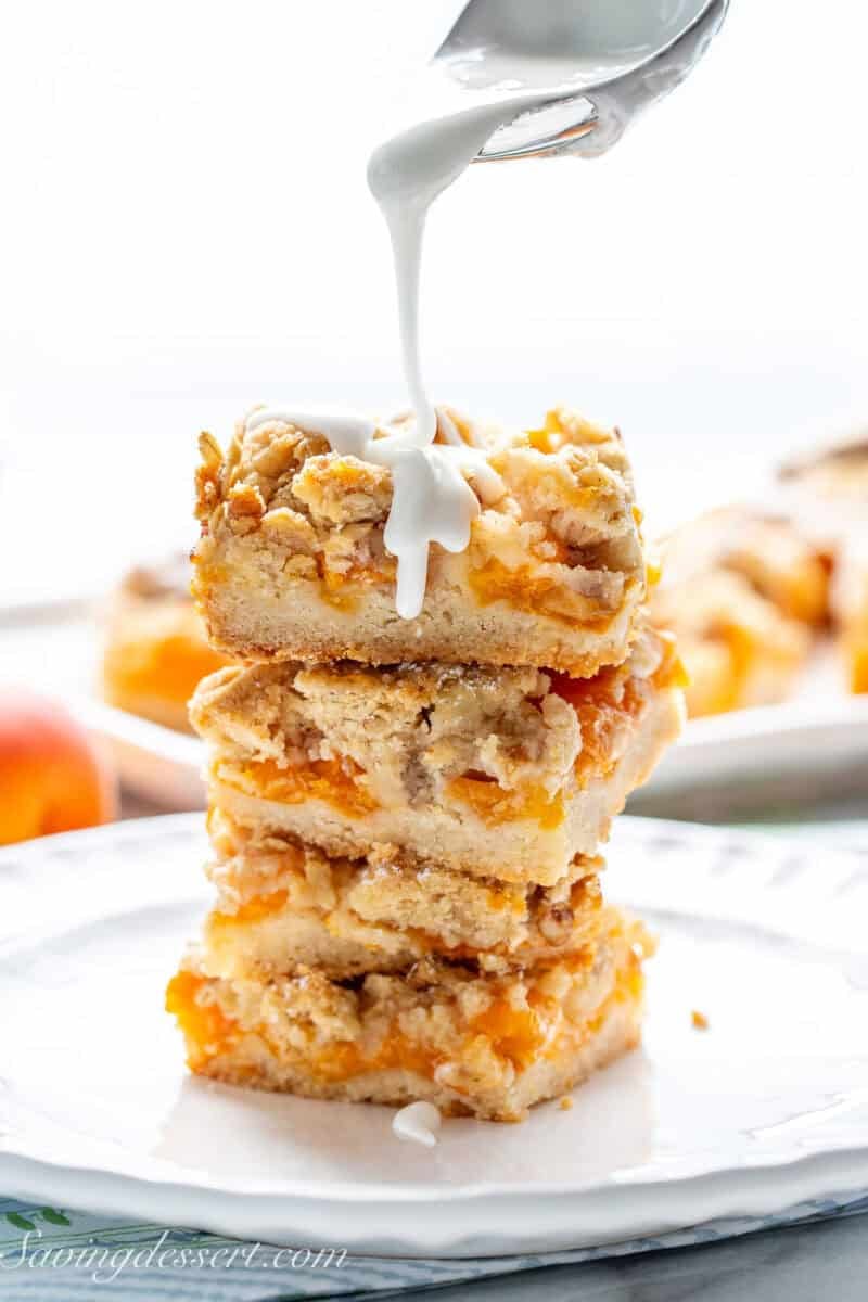 A stack of apricot bars being drizzled with a vanilla icing.