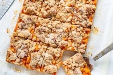 An overhead view of a pan of apricot bars cut into squares with one being lifted out with a spatula.
