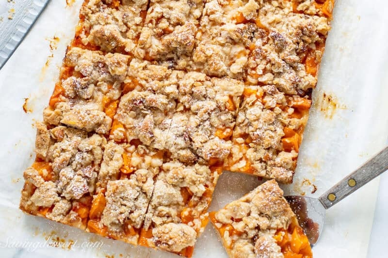 An overhead view of a pan of apricot bars cut into squares with one being lifted out with a spatula.