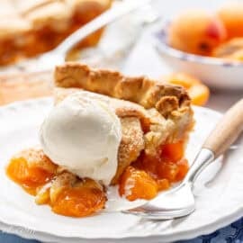 A slice of fresh apricot pie on a plate with a fork and a scoop of vanilla ice cream.