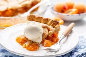 A slice of fresh apricot pie on a plate with a fork and a scoop of vanilla ice cream.