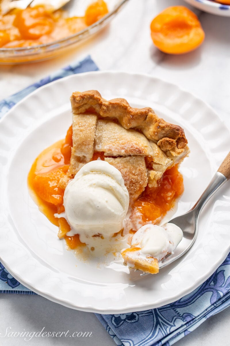 A slice of apricot pie on a plate with a scoop of vanilla ice cream on top.