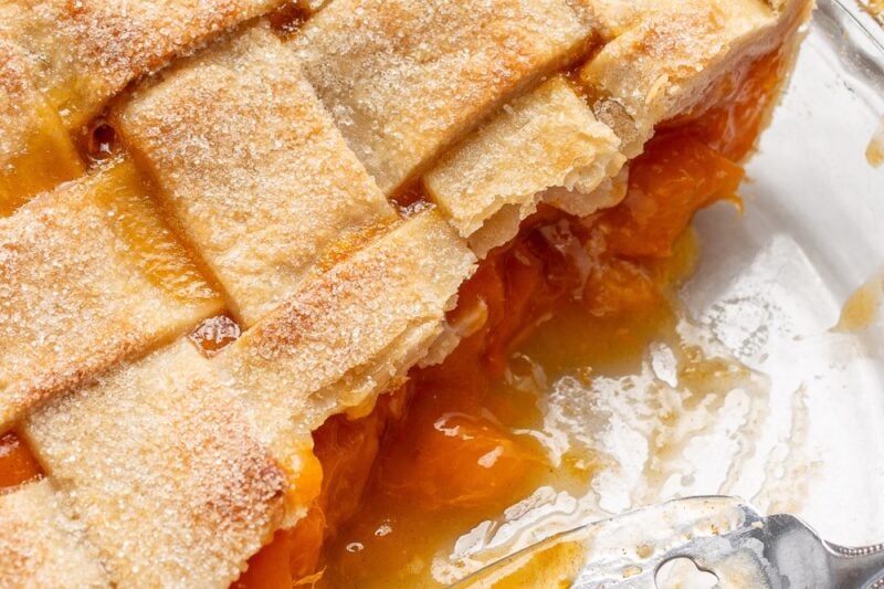 Half a fresh apricot pie in a pie plate with a pie server scooping up the extra filling.
