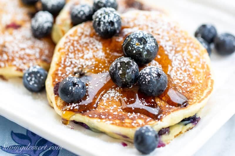 A closeup of a platter of pancakes with blueberries and syrup on top.