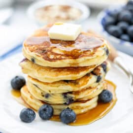 A stack of pancakes with blueberries, butter and syrup.