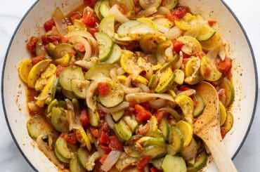 A large skillet filled with summer squash and onions.
