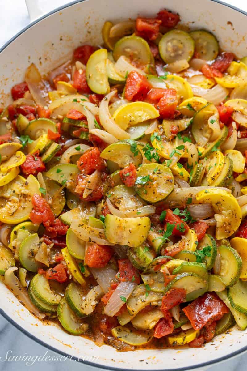 A large skillet filled with Summer squash and onions with tomatoes and loads of seasoning.