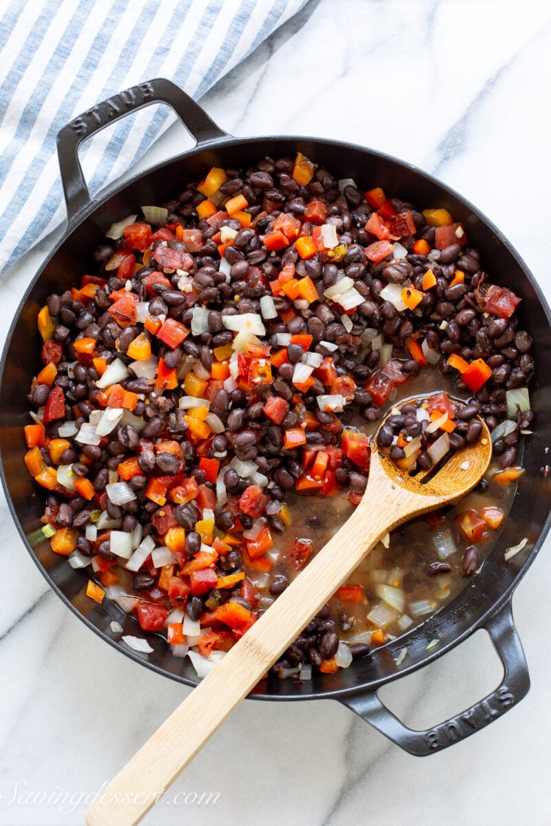 A skillet filled with diced red pepper, onion, tomato and black beans.