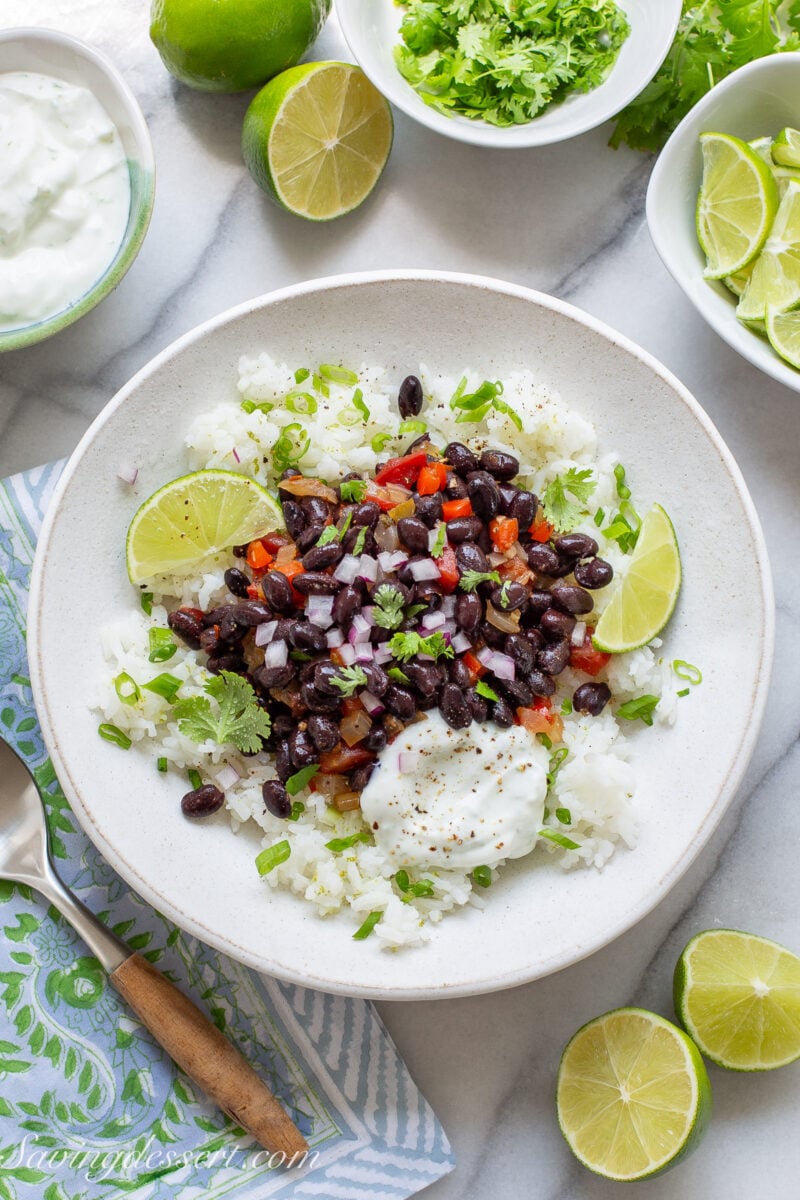 A table with a bowl of white rice with black beans, lime, cilantro and lime crema on the side.