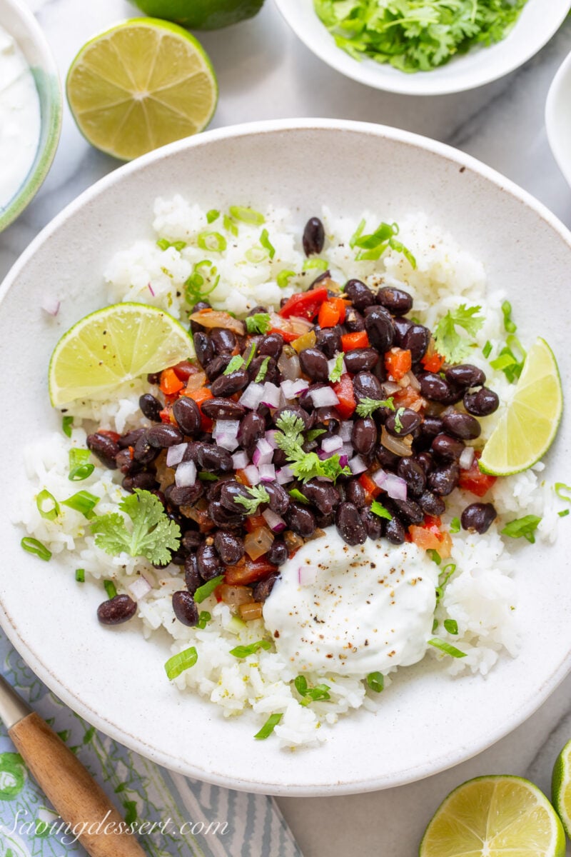 A bowl of black beans and rice with lime wedges and a dollop of lime crema.