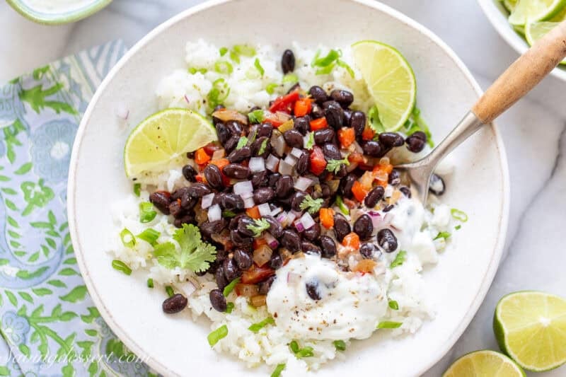 Black beans and rice in a bowl with a spoon and a dollop of lime crema.