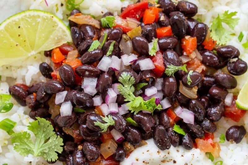 An overhead view of a bowl of white rice with black beans, peppers and onions on top.