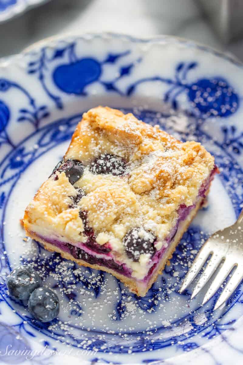 A blueberry crumb bar on a blue and white plate with a small fork.