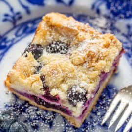 A closeup photo of a blueberry cheesecake bar with a fork on the side.