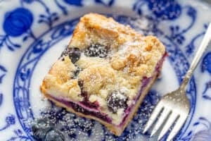A closeup photo of a blueberry cheesecake bar with a fork on the side.