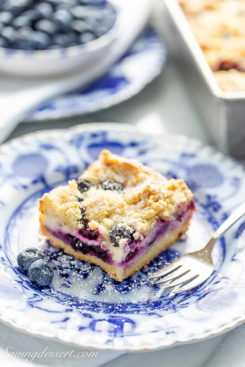 A square piece of blueberry cheesecake crumb bars on a blue plate.