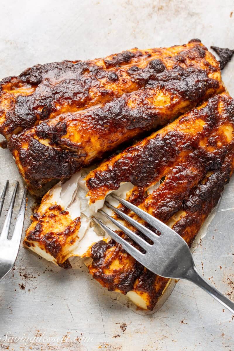 A fish fillet covered with taco seasoning being flaked with a fork.