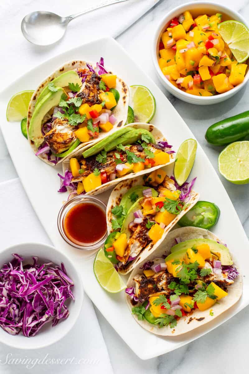 A platter of four fish tacos with purple cabbage, taco sauce and mango salsa.