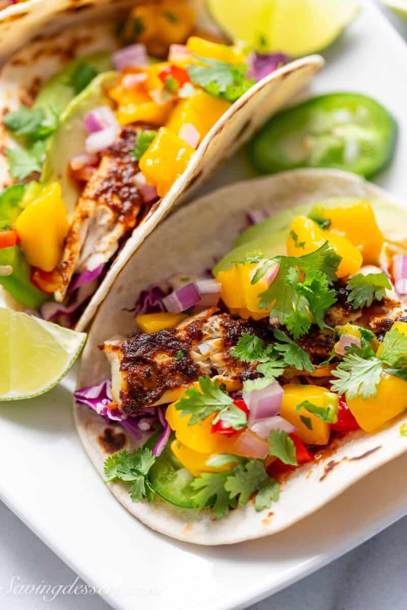 A closeup shot of a fish taco with lime wedges, cilantro and mango salsa.