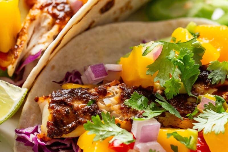 A closeup pictures of a platter of fish tacos topped with mango salsa.