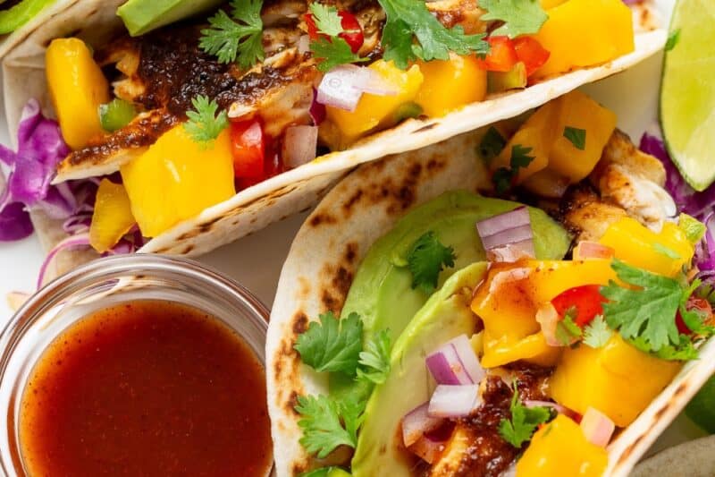 A plate of fish tacos with a bowl of taco sauce on the side.