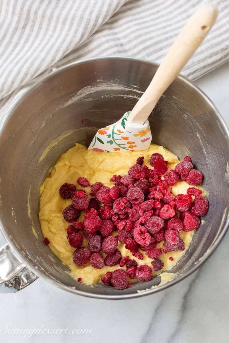 Lemon bars batter in a mixing bowl with frozen raspberries poured in.
