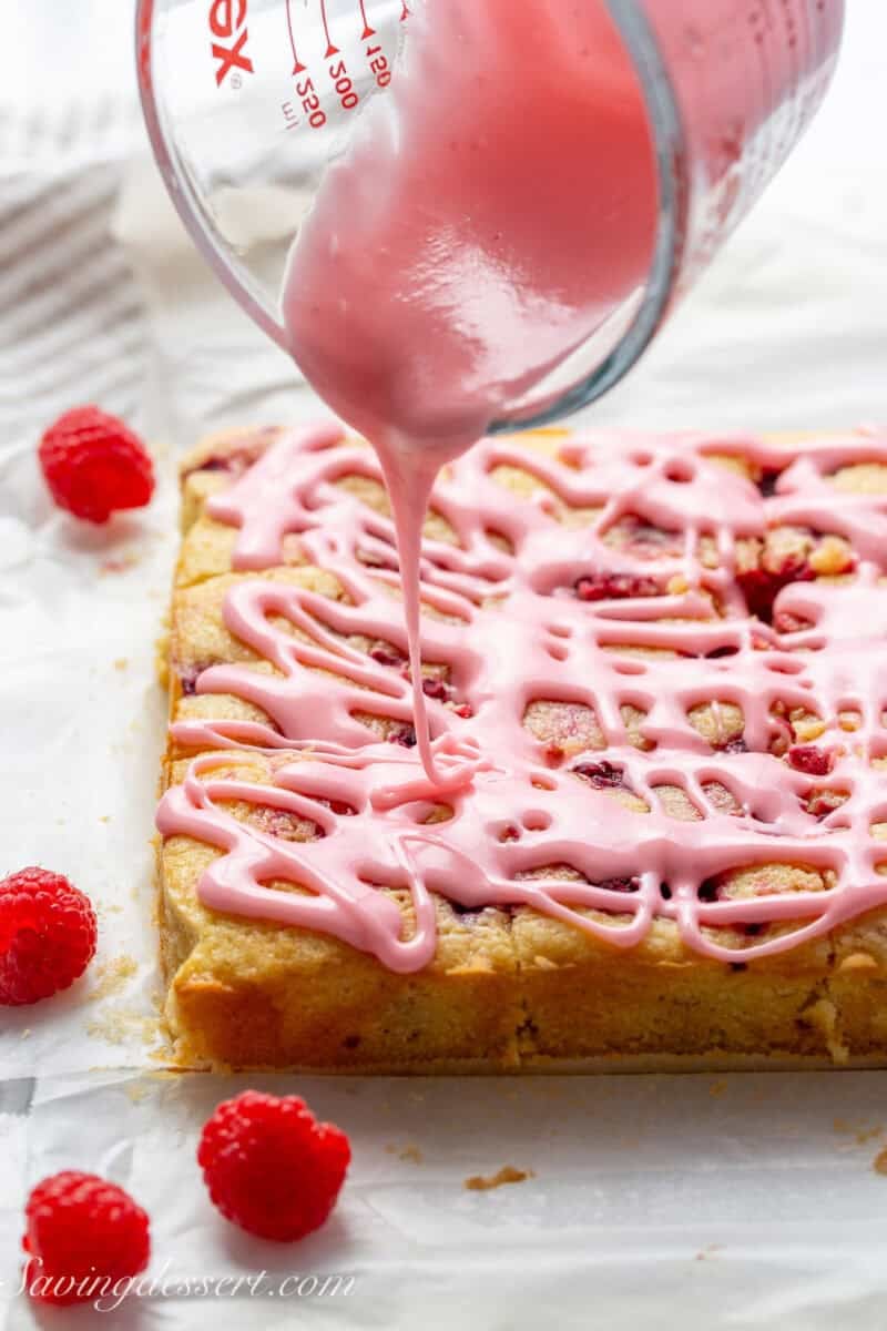 A pan of lemon raspberry blondies being drizzled with a pink raspberry lemon icing.