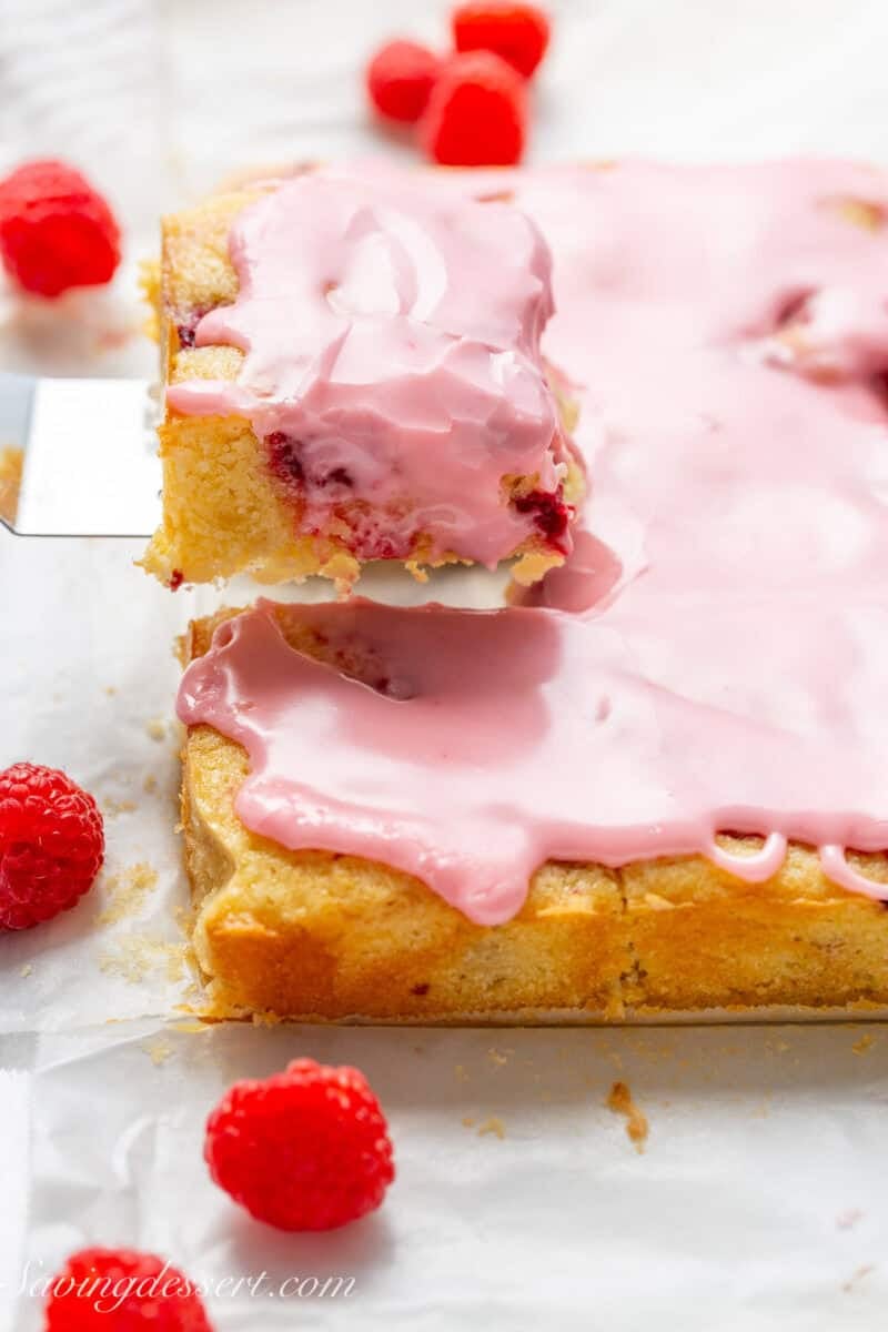 A pan of raspberry bars with one square being lifted out with a spatula.