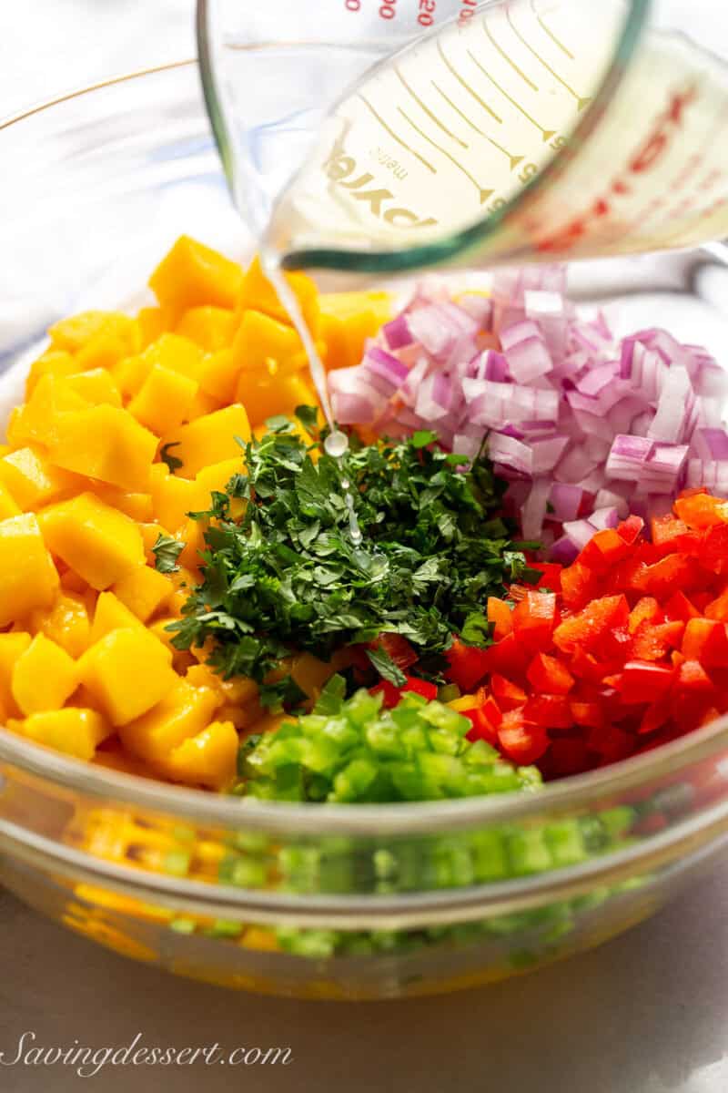 Lime juice being drizzled over a bowl of mango, peppers, onion and cilantro.