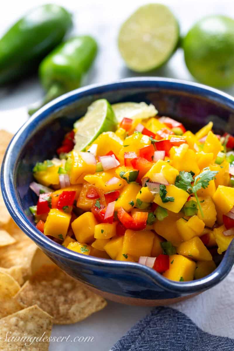 A bowl of chopped mango, peppers, onion and cilantro with limes.