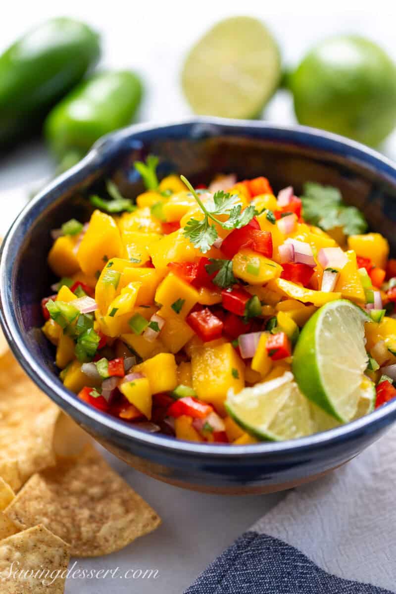 A bowl of mango salsa with limes and chips.