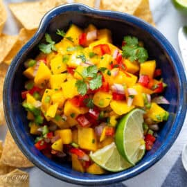 Mango salsa in a bowl with limes, cilantro and chips.