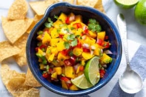 Mango salsa in a bowl with limes, cilantro and chips.