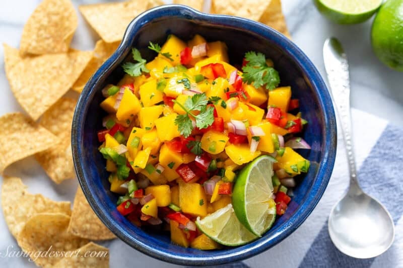 Mango salsa in a bowl with limes, cilantro and chips.