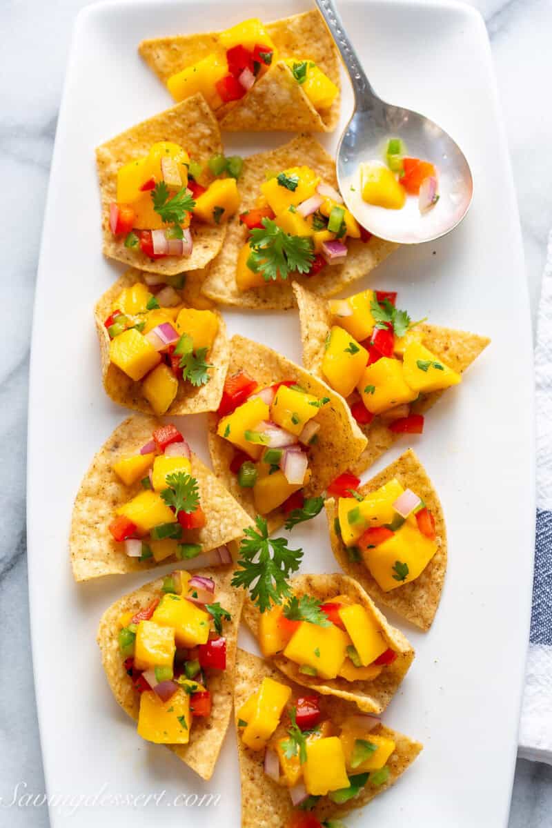 A platter of chips topped with mango salsa with fresh cilantro leaves.